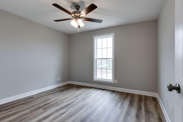 spare room with wood finished floors, a ceiling fan, and baseboards