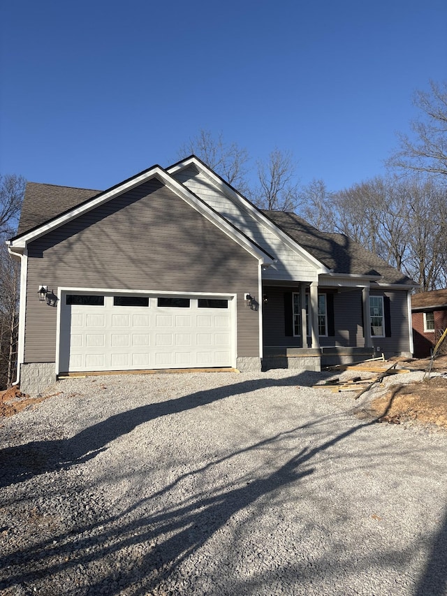 view of front of property featuring a garage, gravel driveway, covered porch, and a shingled roof