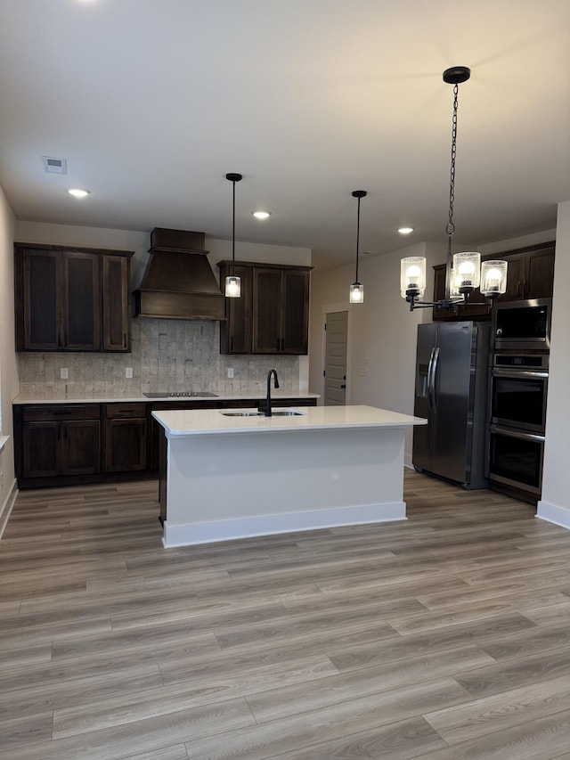 kitchen featuring sink, tasteful backsplash, dark brown cabinets, custom range hood, and stainless steel appliances