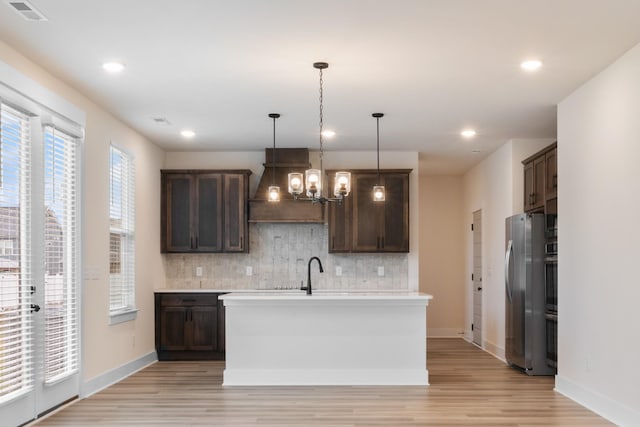 kitchen featuring tasteful backsplash, dark brown cabinets, stainless steel appliances, decorative light fixtures, and a kitchen island with sink