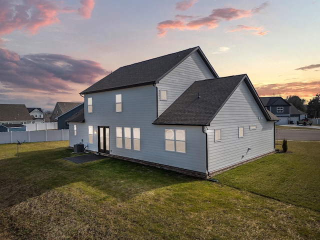 back house at dusk featuring central AC unit and a lawn