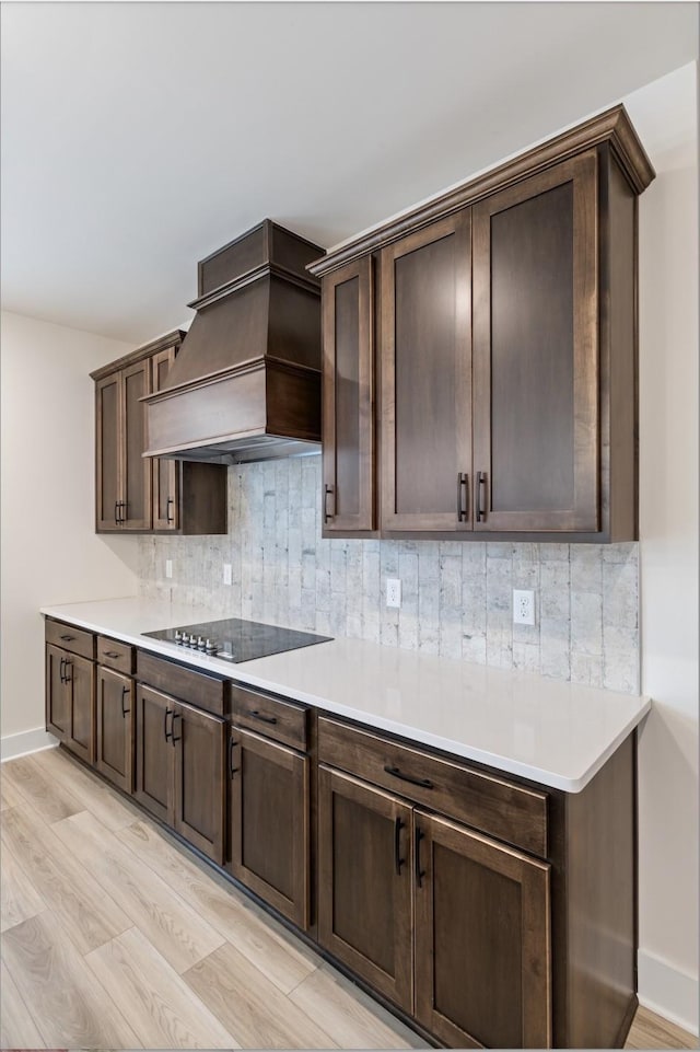 kitchen with premium range hood, dark brown cabinets, black electric stovetop, and decorative backsplash