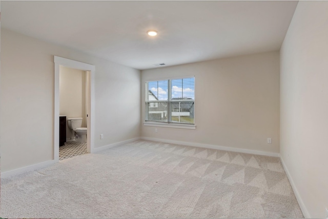 carpeted spare room featuring ensuite bathroom