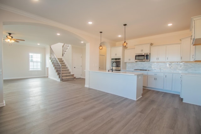 kitchen with white cabinetry, hanging light fixtures, a kitchen island with sink, stainless steel appliances, and light hardwood / wood-style flooring