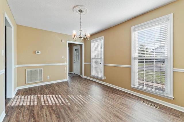 empty room featuring a textured ceiling, a notable chandelier, and dark hardwood / wood-style flooring