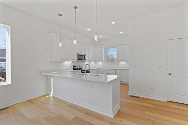 kitchen featuring white cabinets, hanging light fixtures, kitchen peninsula, stainless steel appliances, and light wood-type flooring