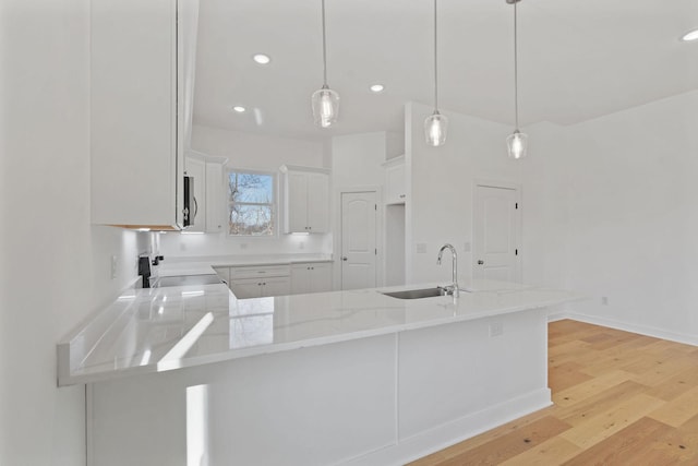 kitchen featuring pendant lighting, sink, kitchen peninsula, and white cabinets