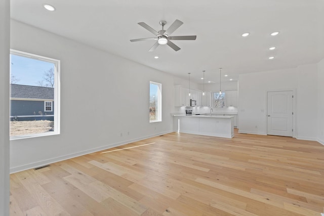 unfurnished living room with ceiling fan, sink, and light wood-type flooring