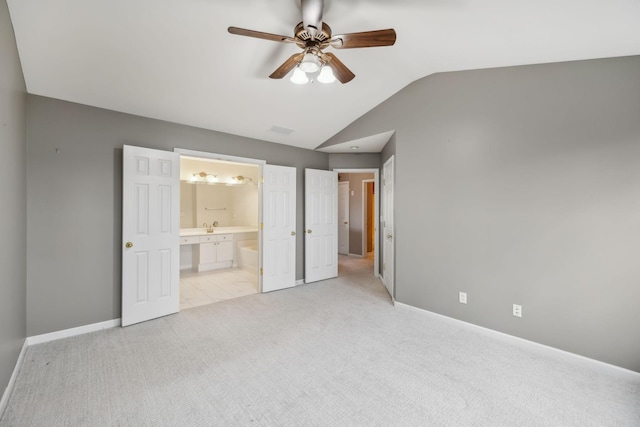 unfurnished bedroom featuring lofted ceiling, sink, ensuite bath, ceiling fan, and light colored carpet