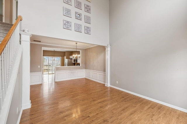 unfurnished living room featuring decorative columns, hardwood / wood-style flooring, a high ceiling, a notable chandelier, and crown molding