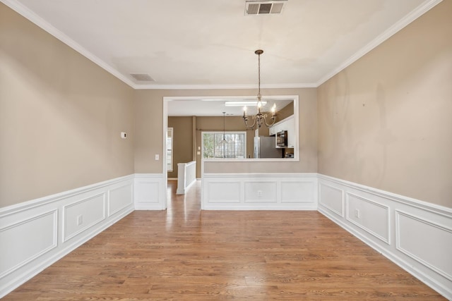 unfurnished dining area with ornamental molding, light wood-type flooring, and a chandelier