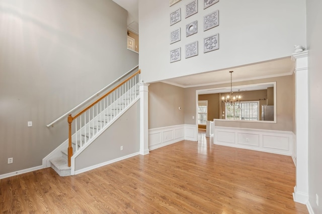 unfurnished living room featuring an inviting chandelier, crown molding, light hardwood / wood-style flooring, and a high ceiling