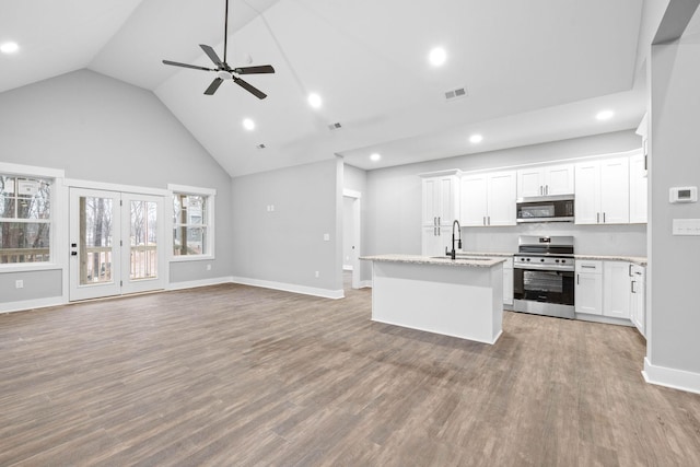 kitchen featuring appliances with stainless steel finishes, a kitchen island with sink, hardwood / wood-style floors, light stone counters, and white cabinets