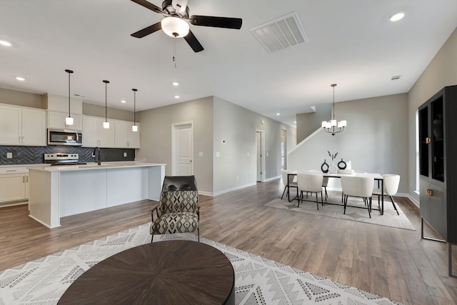 kitchen with pendant lighting, appliances with stainless steel finishes, white cabinetry, light hardwood / wood-style floors, and an island with sink