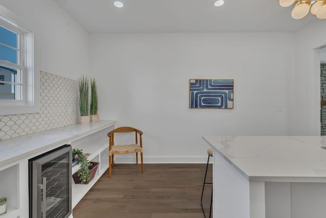 kitchen featuring a breakfast bar, dark hardwood / wood-style floors, beverage cooler, light stone countertops, and decorative backsplash