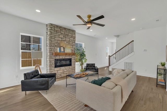 living room with ceiling fan, a stone fireplace, and light wood-type flooring