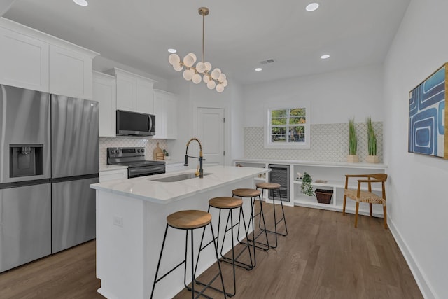 kitchen with white cabinetry, sink, hanging light fixtures, a kitchen island with sink, and stainless steel appliances