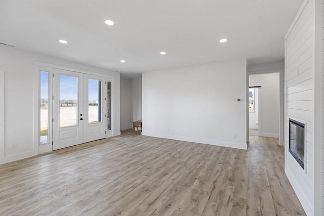 unfurnished living room featuring light hardwood / wood-style flooring, a large fireplace, and french doors