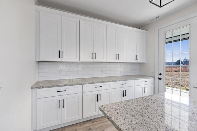 kitchen featuring light stone counters, light hardwood / wood-style flooring, decorative backsplash, and white cabinets