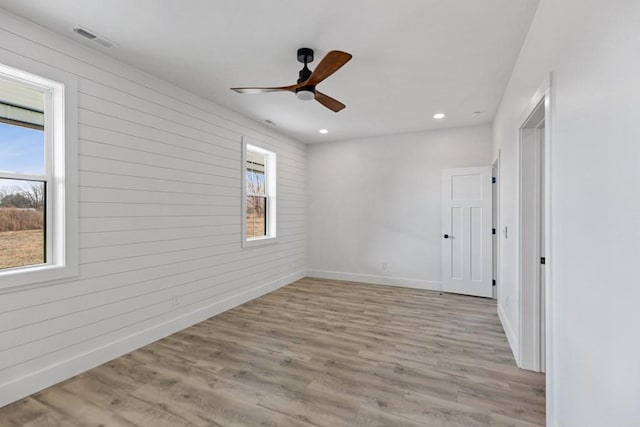 unfurnished room with a wealth of natural light, wooden walls, ceiling fan, and light wood-type flooring
