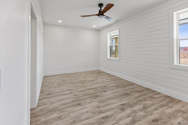 spare room featuring light hardwood / wood-style flooring, wooden walls, and ceiling fan