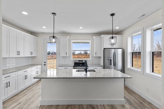 kitchen with appliances with stainless steel finishes, sink, white cabinets, hanging light fixtures, and a kitchen island with sink