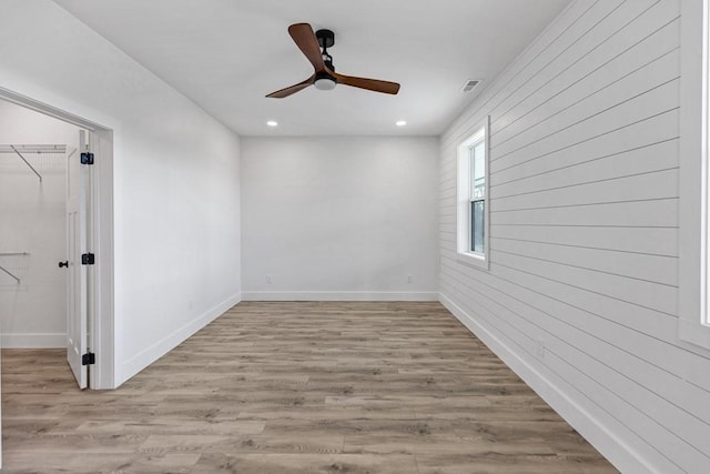 unfurnished room featuring ceiling fan, light wood-type flooring, and wood walls