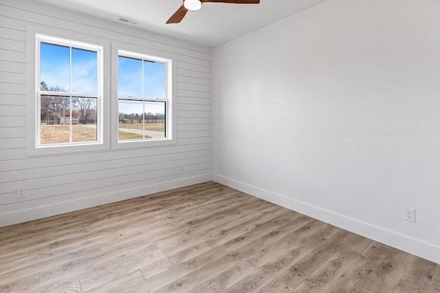 empty room featuring ceiling fan, light wood-type flooring, and wood walls
