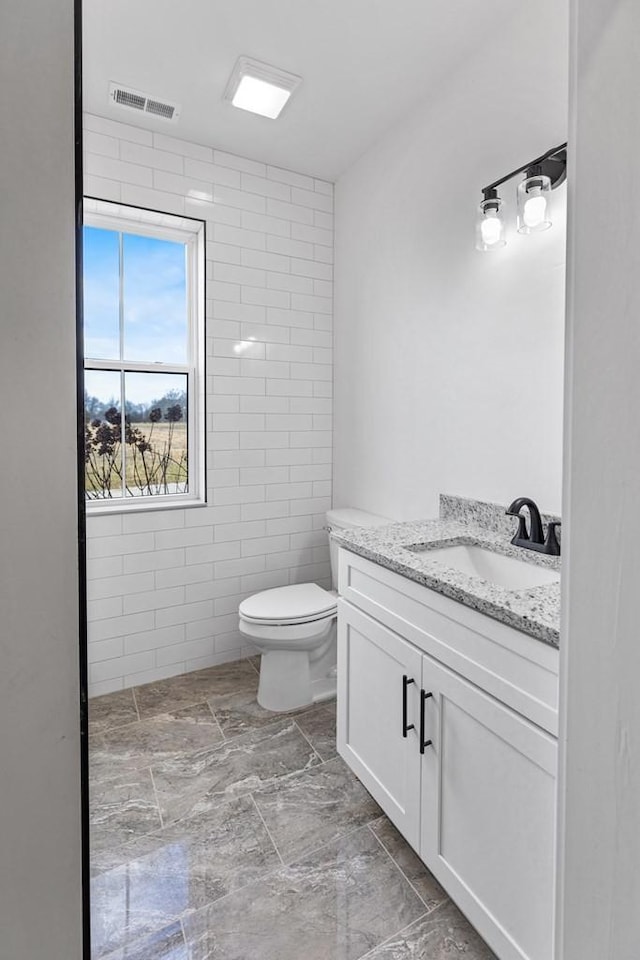 bathroom with vanity, tile walls, and toilet