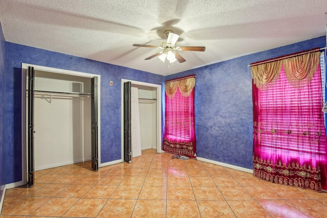 unfurnished bedroom featuring multiple closets, ceiling fan, a textured ceiling, and light tile patterned floors