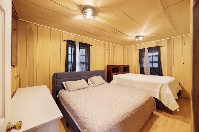 bedroom with light hardwood / wood-style flooring, multiple windows, and wooden walls