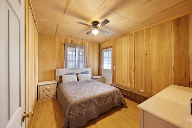 bedroom with ceiling fan, light hardwood / wood-style floors, and wood walls