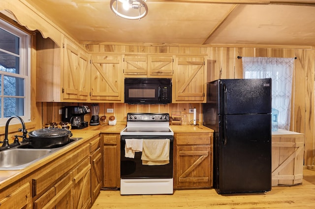 kitchen featuring wood walls, light hardwood / wood-style floors, sink, and black appliances