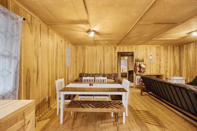 dining room with electric panel, light wood-type flooring, and wood walls