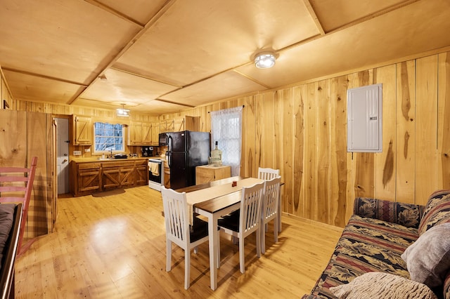 dining area featuring sink, wooden walls, electric panel, and light wood-type flooring