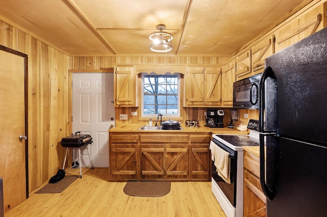 kitchen featuring light wood-type flooring, wood walls, sink, and black appliances