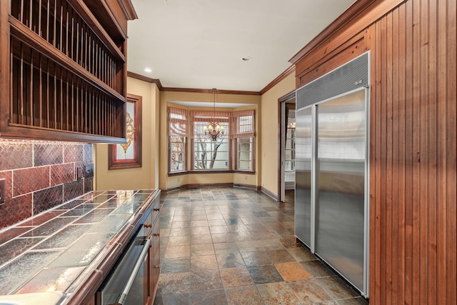 kitchen with pendant lighting, stainless steel built in refrigerator, backsplash, tile counters, and a notable chandelier