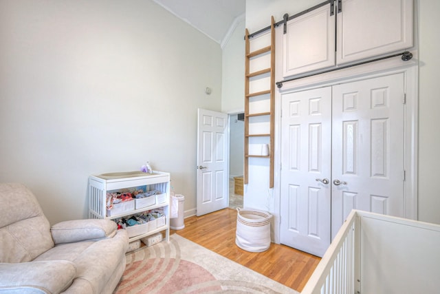 bedroom featuring lofted ceiling, crown molding, light hardwood / wood-style floors, a barn door, and a closet