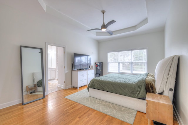 bedroom with light hardwood / wood-style floors, a raised ceiling, ceiling fan, and ensuite bathroom