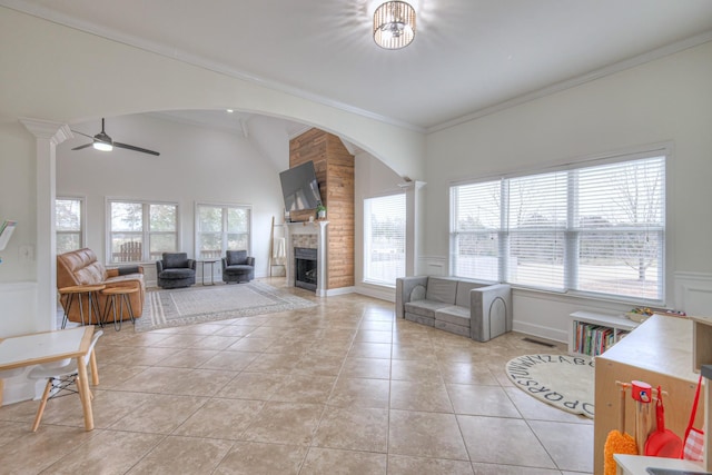 tiled living room with crown molding, ceiling fan, a towering ceiling, decorative columns, and a fireplace