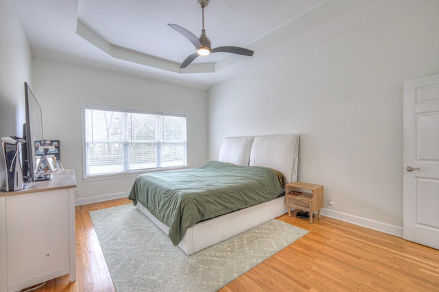 bedroom with a tray ceiling, light hardwood / wood-style flooring, and ceiling fan