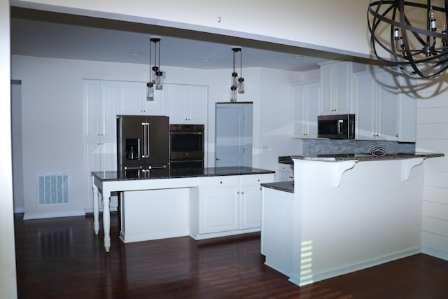 kitchen featuring stainless steel appliances, white cabinetry, a kitchen island, and dark stone countertops