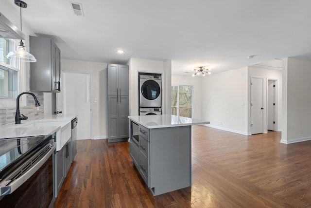 kitchen with decorative light fixtures, stacked washer / drying machine, gray cabinets, light countertops, and visible vents