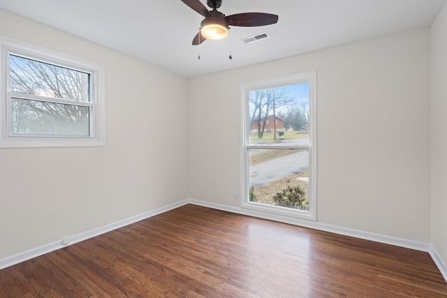 empty room with baseboards, visible vents, ceiling fan, and dark wood-type flooring