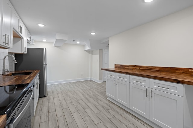 kitchen with tasteful backsplash, white cabinetry, a sink, and wood counters