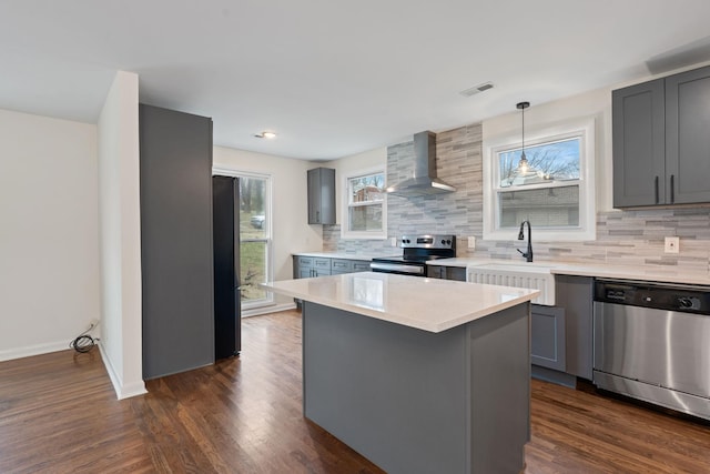 kitchen with stainless steel appliances, a kitchen island, light countertops, gray cabinets, and wall chimney exhaust hood