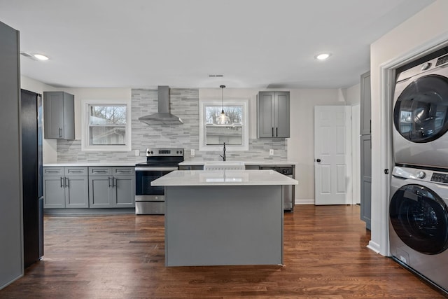 kitchen with stainless steel appliances, stacked washer and dryer, light countertops, hanging light fixtures, and wall chimney range hood