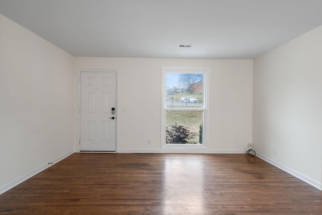 spare room with dark wood-type flooring, visible vents, and baseboards