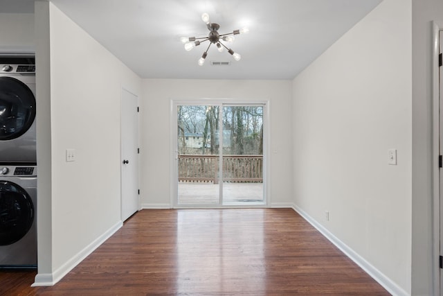 unfurnished dining area featuring dark wood-type flooring, stacked washer / drying machine, visible vents, and baseboards