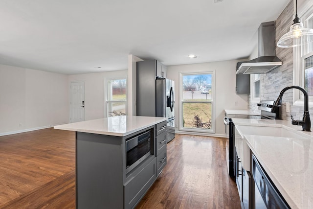 kitchen featuring appliances with stainless steel finishes, gray cabinets, a center island, wall chimney exhaust hood, and decorative light fixtures